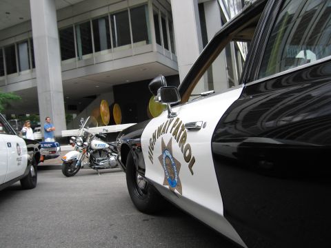 1991 Ford LTD Crown Victoria - Side profile of a black-and-white California Highway Patrol cruiser door and star emblem, with a police motorcycle parked in the background.