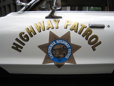 1991 Ford LTD Crown Victoria - Close-up of a white police car door bearing the gold HIGHWAY PATROL lettering and California Highway Patrol star badge.