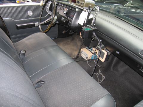 1991 Ford LTD Crown Victoria - Interior of a vintage sedan with a vinyl bench seat, steering wheel and a dashboard-mounted two-way radio with coiled cords.
