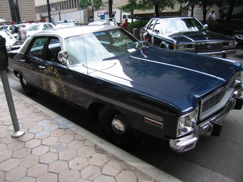 1991 Ford LTD Crown Victoria - dark blue 1970s Dodge full-size patrol sedan with spotlight and star door emblem parked among other police cars at a show.