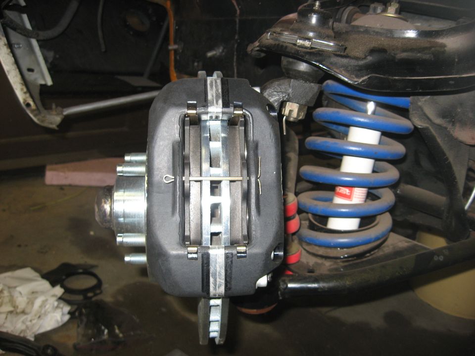 Close-up of a vehicle's front brake caliper, rotor, and blue coil spring.
