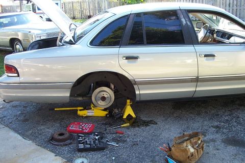 1992 Ford Crown Victoria - A car is up on a jack with its wheel removed, surrounded by tools, indicating maintenance is underway.