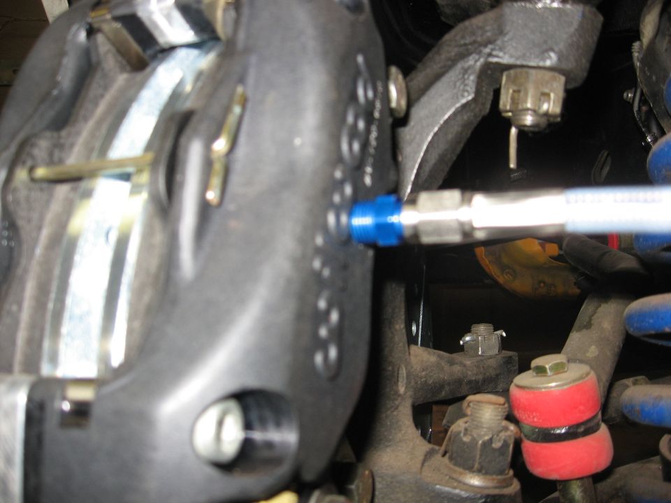 Close-up of a car brake caliper with a tool on the bleeder valve.