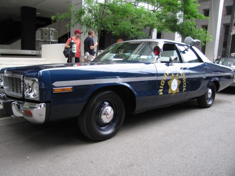 1991 Ford LTD Crown Victoria - Side view of a blue-and-white 1970s full-size patrol sedan with a gold star door emblem and spotlight, parked at a car show.