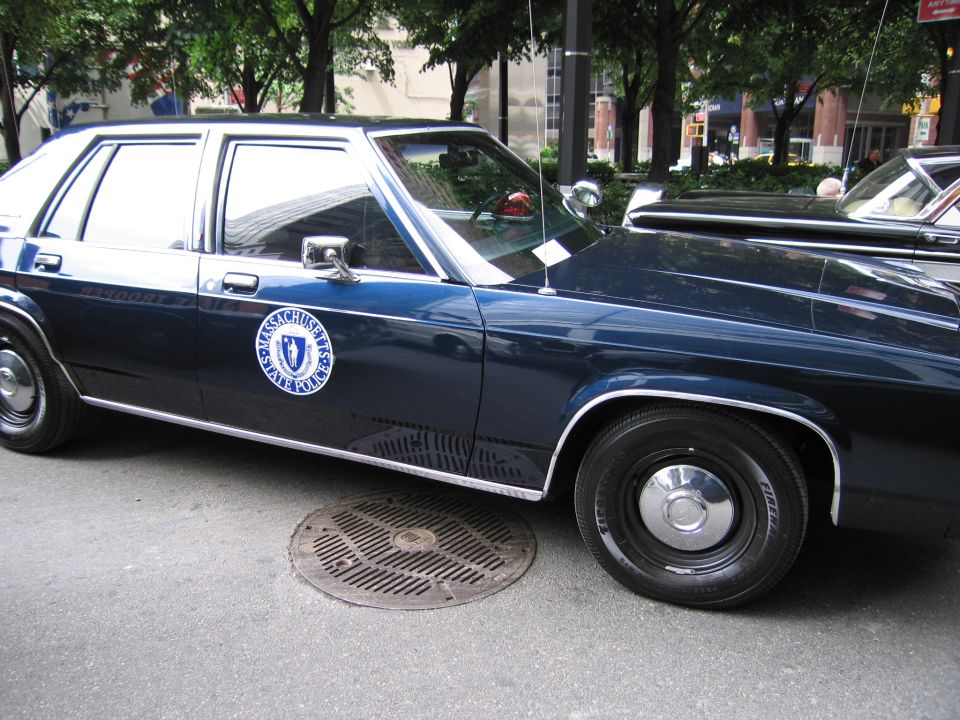 Side of dark blue Massachusetts State Police Ford sedan with seal on door