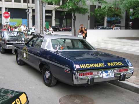 1991 Ford LTD Crown Victoria - dark blue Dodge sedan with gold HIGHWAY PATROL lettering and a WHP plate parked on a downtown street as a man photographs it.
