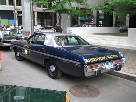 1991 Ford LTD Crown Victoria - dark blue Dodge HIGHWAY PATROL sedan with spotlight and gold star emblem parked along a curb beside other vintage police cars.