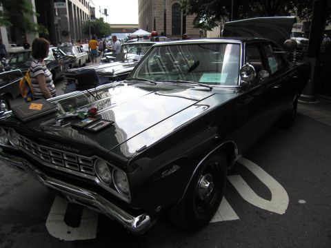 1991 Ford LTD Crown Victoria - black 1960s Plymouth Satellite with chrome grille and dual exhausts displayed at an outdoor car show with spectators nearby.