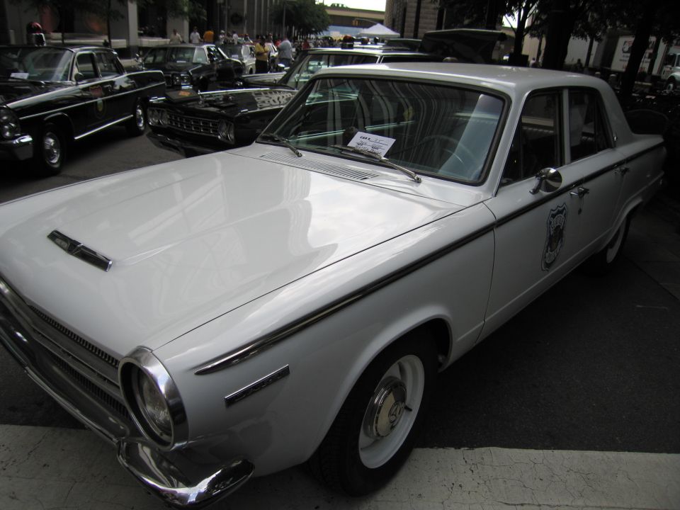 Front three-quarter of white 1960s Dodge Dart police sedan with door badge