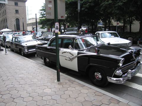 1991 Ford LTD Crown Victoria - black-and-white 1950s Ford sedan lettered BUREAU OF POLICE parked along a curb beside other vintage police cars at a show.