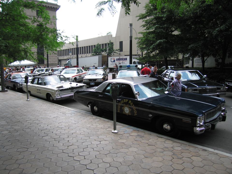 Row of vintage police cars including black-and-white highway patrol sedan along curb
