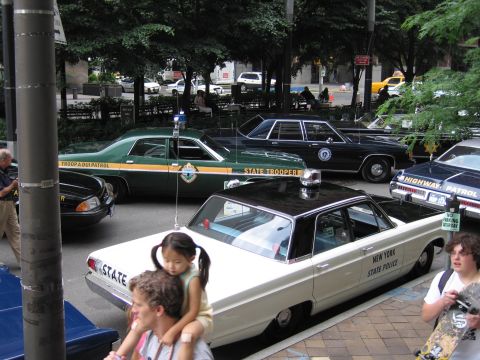 1991 Ford LTD Crown Victoria - Vintage New York State Police and state trooper sedans, including green and white cars, on display while a man carries a child nearby.
