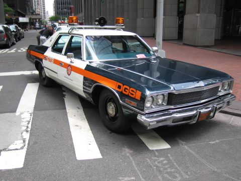 1991 Ford LTD Crown Victoria - restored dark blue and orange DGS official sedan with a roof light bar and siren sits on a city crosswalk.