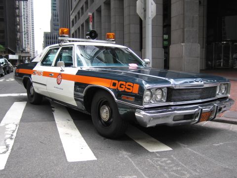 1991 Ford LTD Crown Victoria - vintage DGS official sedan painted dark blue with an orange stripe and roof lights is parked on a downtown crosswalk.