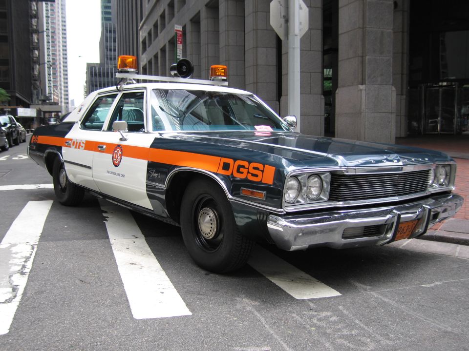 Blue and orange DGS official sedan with roof lights parked on a downtown street