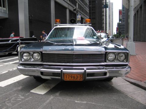 1991 Ford LTD Crown Victoria - chrome front grille of a dark Plymouth official sedan with roof lights and an NY official license plate, photographed head-on.
