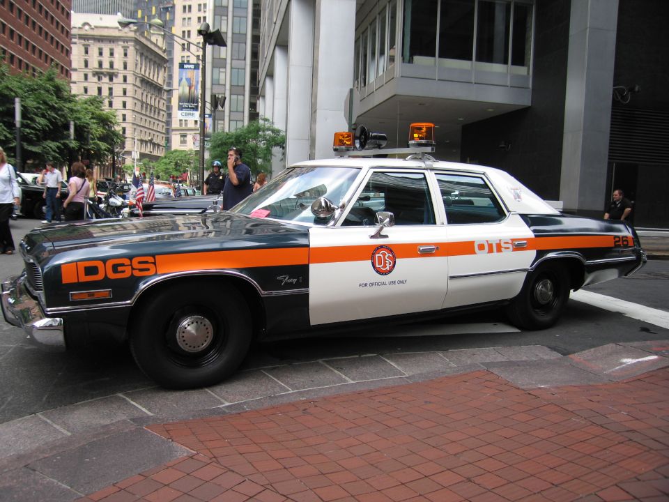 Side view of a blue and orange DGS official sedan parked on a brick plaza