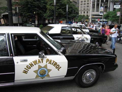 1991 Ford LTD Crown Victoria - Black and white Ford California Highway Patrol cruisers with the CHP star emblem are parked in a row on a downtown street.