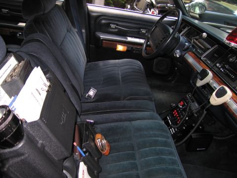 1991 Ford LTD Crown Victoria - dark blue front bench seat of a vintage police car with mounted radio gear, paperwork and a holstered object on the seat.