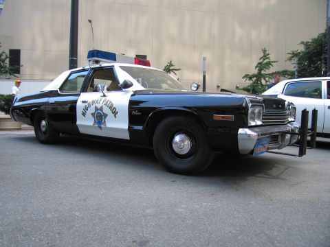 1991 Ford LTD Crown Victoria - Front three-quarter of a black-and-white Dodge Highway Patrol sedan with a gold star emblem, push bar, and roof lights on a city street.