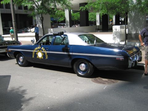 1991 Ford LTD Crown Victoria - Rear three-quarter of a dark blue Highway Patrol sedan with white roof and gold star emblem on the door, parked on a city street.