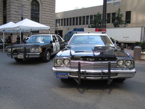 1991 Ford LTD Crown Victoria - Two black-and-white police cars parked under a tent, the nearer a Dodge with a chrome front push bar and California plate.