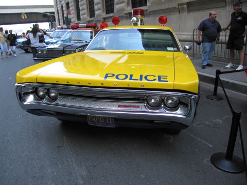 1991 Ford LTD Crown Victoria - Front view of a yellow Plymouth POLICE sedan with twin red roof beacons and a PAPD 71 plate, behind a stanchion rope on a city street.