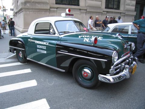 1991 Ford LTD Crown Victoria - green and black vintage coupe lettered Emergency Service Division and POLICE N.Y., with a white roof and red dome light, parked downtown.