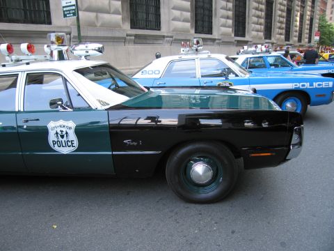 1991 Ford LTD Crown Victoria - classic green-and-white NYPD police car with City of New York Police shield decal parked in front of a blue cruiser on a city street.
