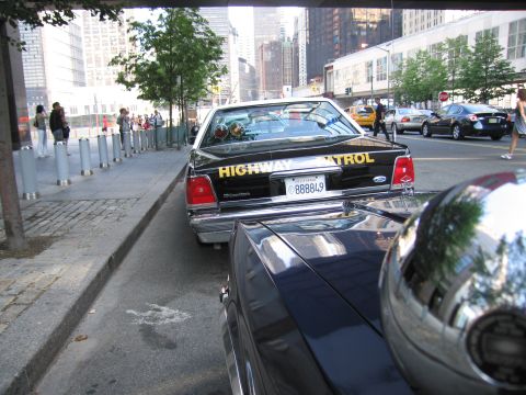 1991 Ford LTD Crown Victoria - Rear three-quarter view of a black Highway Patrol sedan with plate 888849, parked along a sidewalk among pedestrians and traffic.