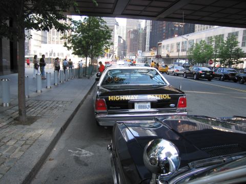 1991 Ford LTD Crown Victoria - black Highway Patrol sedan with plate 888849 parked along a downtown curb beside a tree, with pedestrians and traffic nearby.