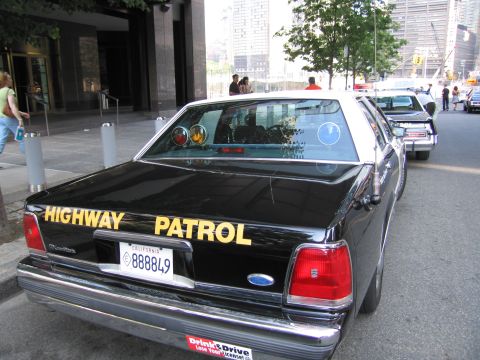 1991 Ford LTD Crown Victoria - Rear of a black police sedan lettered Highway Patrol with California plate 888849 and a bumper sticker, parked on a city street.