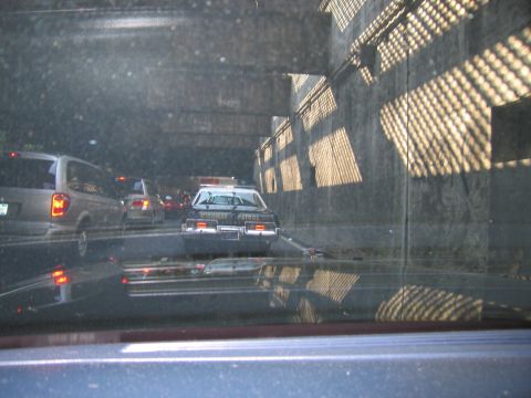 1991 Ford LTD Crown Victoria - View through a windshield of a police car with lightbar sitting in slow tunnel traffic beside concrete walls.
