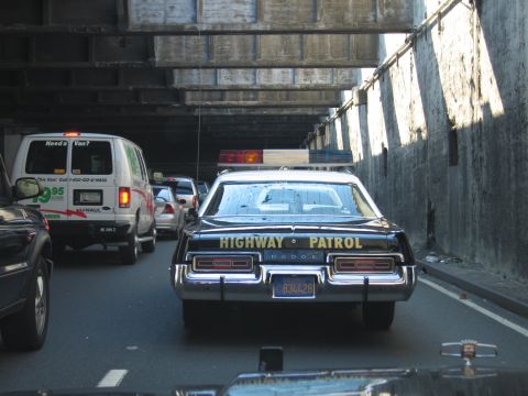 1991 Ford LTD Crown Victoria - black Dodge Highway Patrol cruiser with plate 834428 sits in tunnel traffic next to a green-and-white U-Haul van.