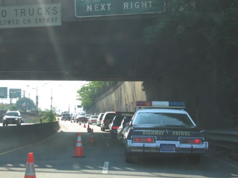 1991 Ford LTD Crown Victoria - black Highway Patrol sedan with lightbar parked at a coned-off roadwork lane beneath a Next Right highway overpass sign.