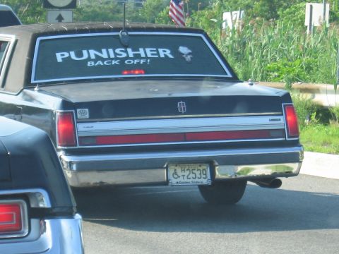 1991 Ford LTD Crown Victoria - Rear of a black Lincoln sedan with a PUNISHER BACK OFF! rear-window decal and a New Jersey Garden State plate on a roadway.