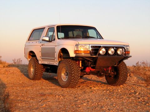 1996 Ford Bronco - A modified 1996 Ford Bronco sits on a dusty incline under a clear sky, its off-road enhancements visible.