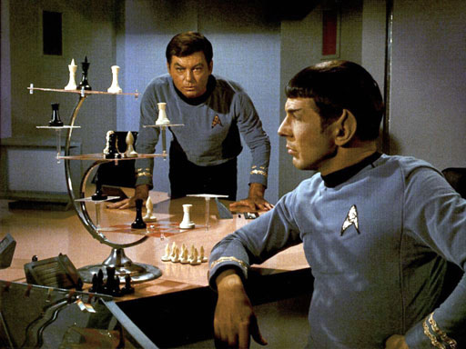 Two men in blue uniforms play a futuristic chess game