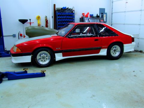 1990 Ford Mustang - A red and white 1990 Ford Mustang is parked in a garage with a grey hood and racing wheels.
