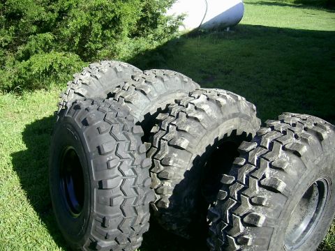 1978 Ford Bronco - Several large off-road tires are displayed outdoors on a sunny day.