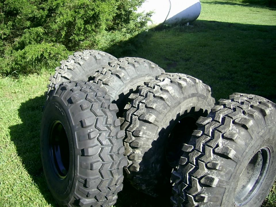 Four off-road tires with aggressive tread patterns are arranged on grass