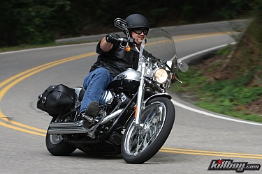 1996 Ford Crown Victoria - Motorcyclist navigates a curve on a scenic road, wearing a helmet and leather vest.