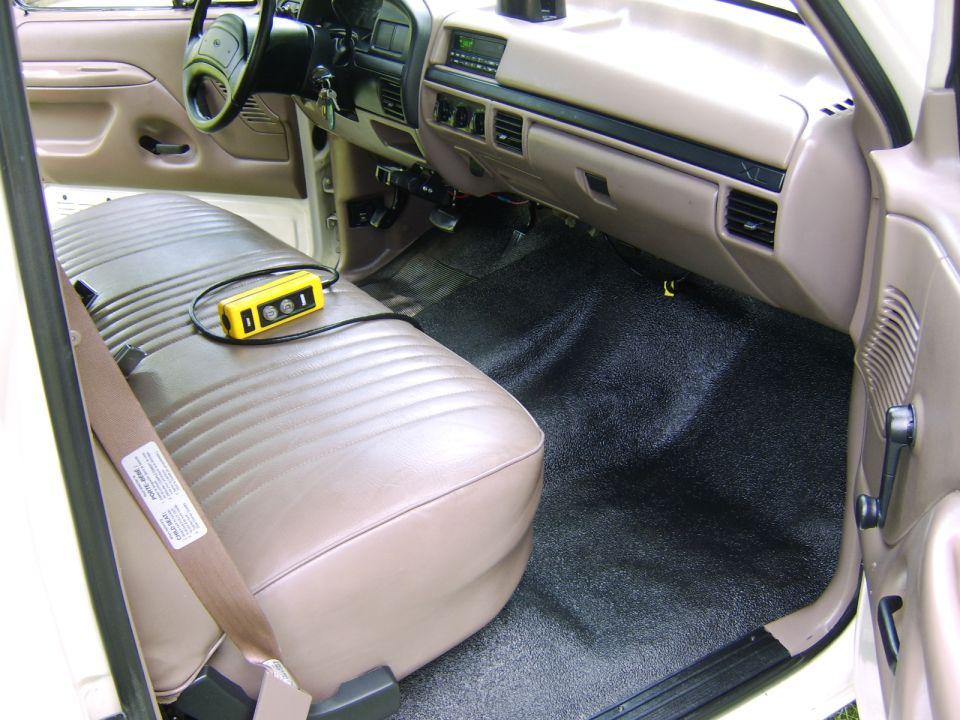 Tan cloth bench seat interior of a Ford truck cab with dash, vents and carpeted floor