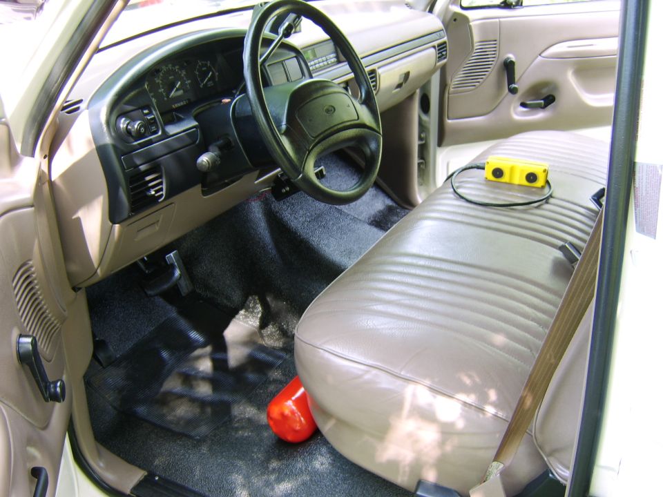 Tan truck cab interior with bench seat, steering wheel, and yellow device on seat