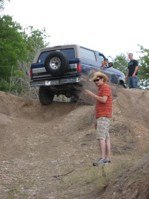 1996 Ford Bronco - A blue 1996 Ford Bronco navigates an off-road trail, with a man in a cowboy hat observing the climb.