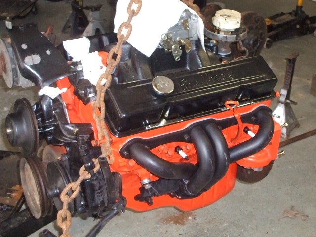 V8 engine block painted orange, black valve covers, black headers, and a chain hoist attached