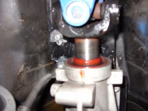 1978 Ford Mustang II - Tight close-up under a car showing a polished steel shaft passing through a bearing seated in a red-orange seal, clamped by a cast aluminum…