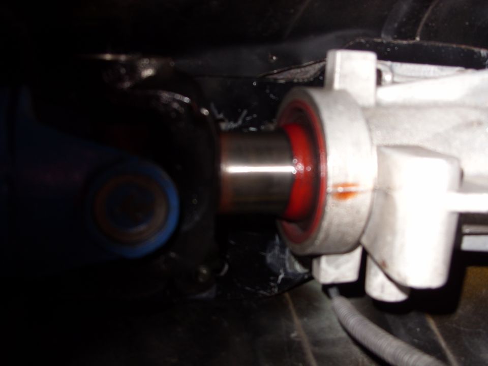 Driveshaft slip yoke entering white-painted transmission tail housing with red seal, underside view