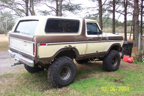 Brown and tan Ford Bronco with lifted suspension and large tires parked on grass
