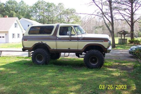 1979 Ford Bronco parked on grass, side view. Beige and brown two-tone paint, lifted suspension with large tir…